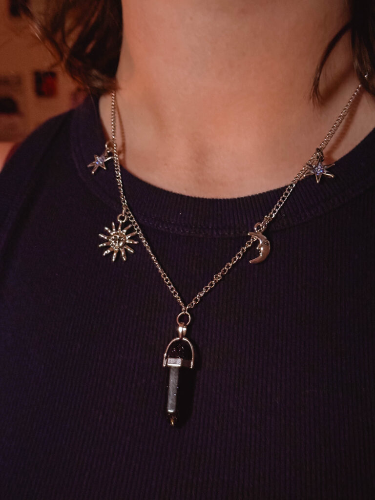 Celestial charm necklace worn with a dark top—featuring silver moon, sun, star charms, and a black crystal pendant for a dreamy, handmade look