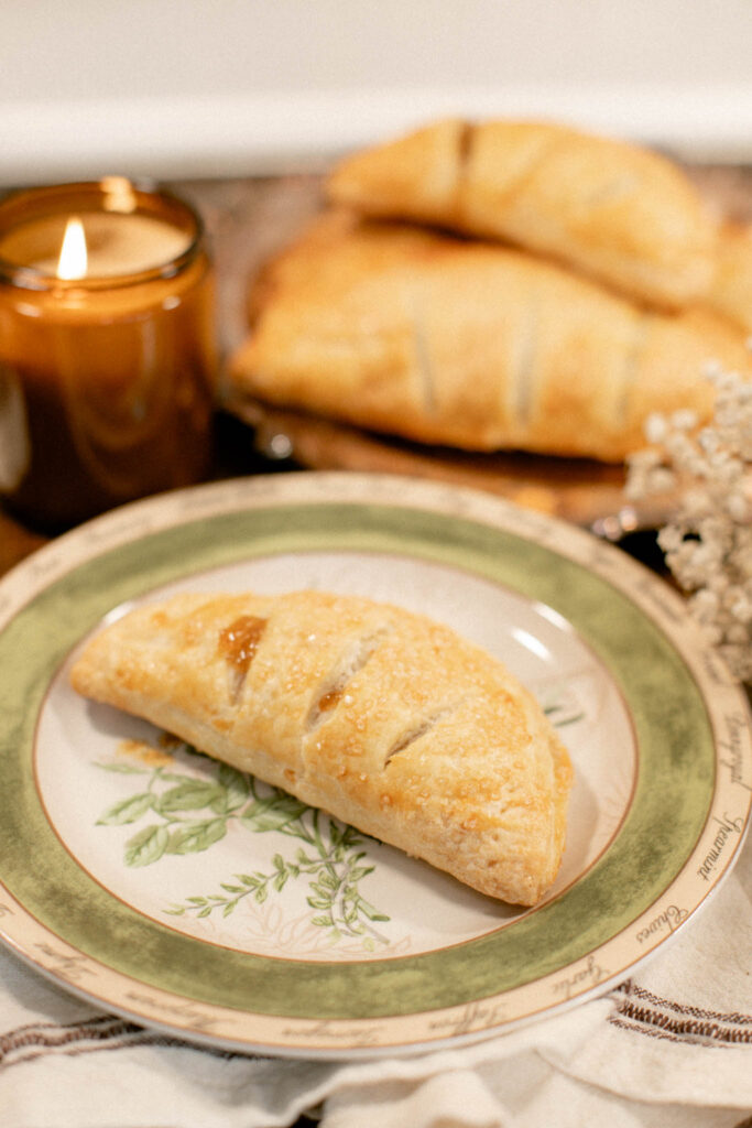 Close-up of a sugared apple hand pie on a green-trimmed plate beside a glowing amber candle.