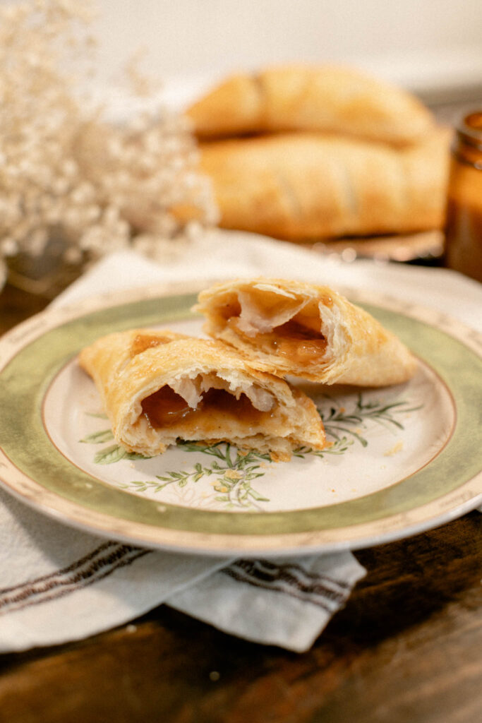 Apple hand pie split open to reveal gooey cinnamon-apple filling on a vintage botanical plate.