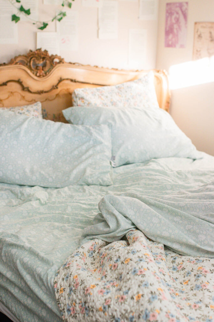 Soft, light blue floral bedding on a cozy bed with an antique headboard, sunlight filling a calm and whimsical bedroom.